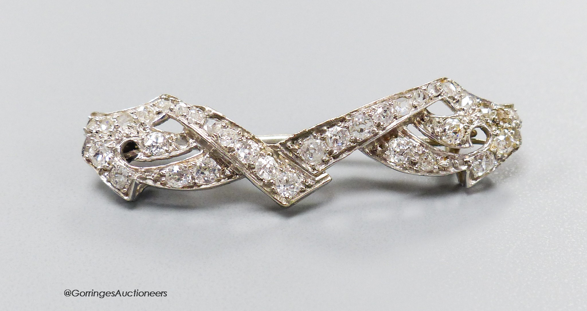 A white metal and diamond cluster set shaped bar brooch, 38mm, gross weight 4 grams.